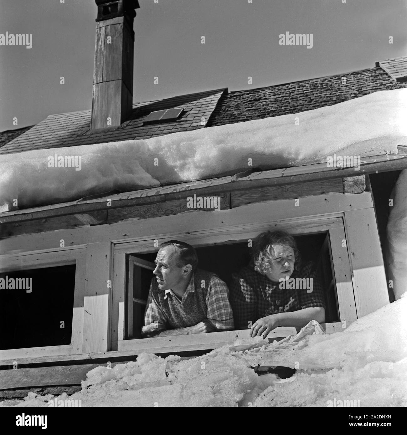 Eine Frau und ein Mann schauen aus ihrem Dachfenstern, Deutschland 1930er Jahre. A man and a woman looking out of their roof window, Germany 1930s. Stock Photo