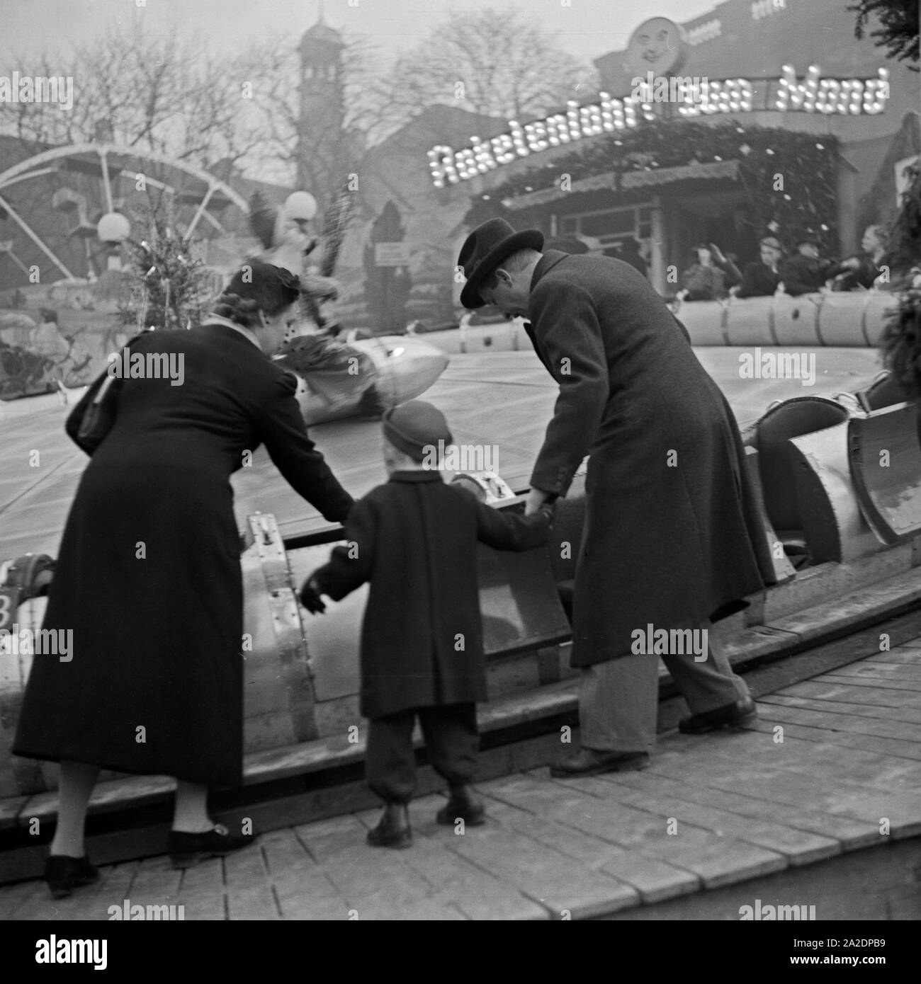 Ein kleiner Junge steht mit seinen Eltern an einer Berg und Talbahn auf dem Weihnachtsmarkt, Deutschland 1930er Jahre. A little boy and his parents at a music express fairground ride at the christmas market, Germany 1930s. Stock Photo