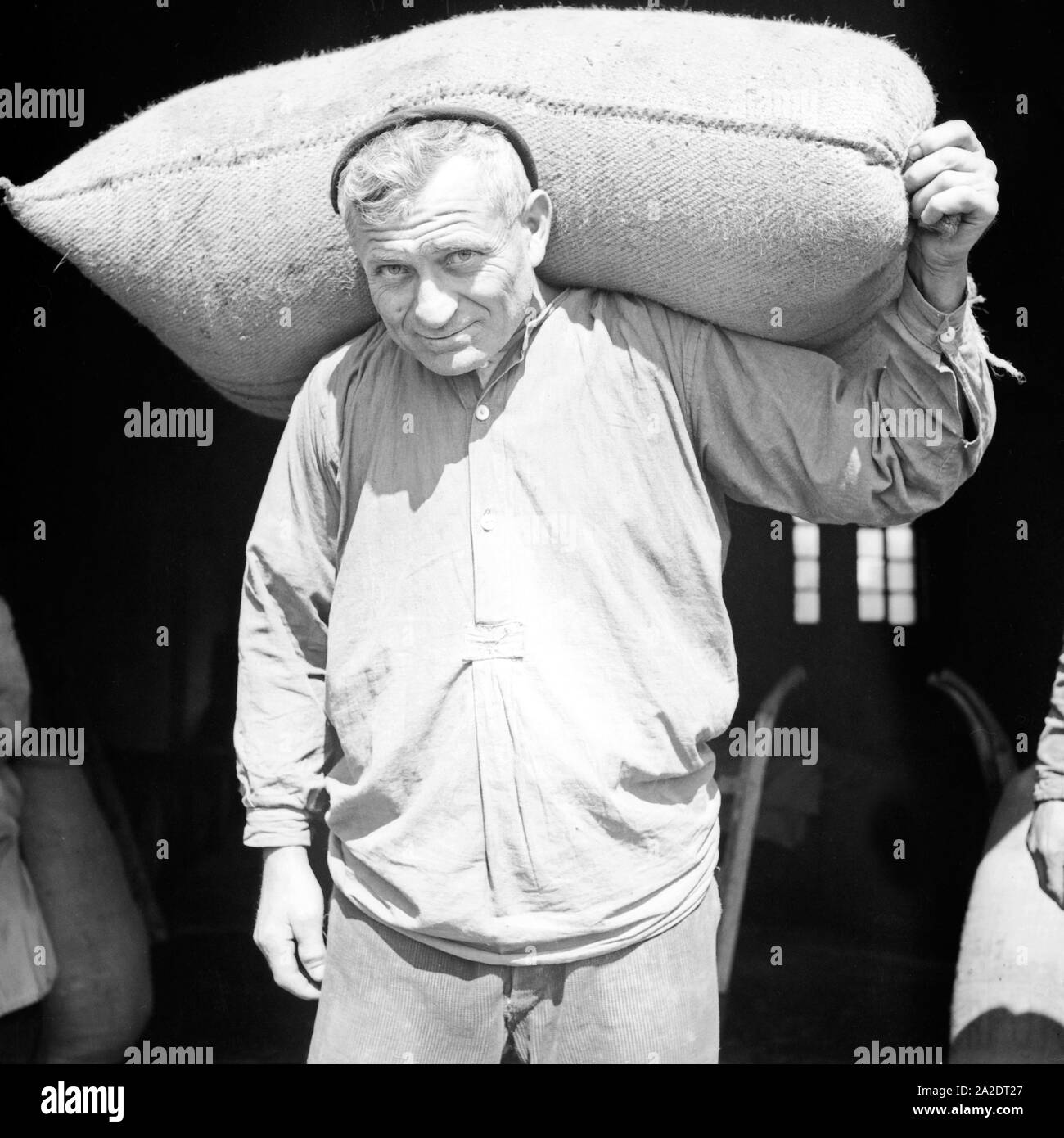 Ein Lagerarbeiter schleppt einen Sack aus dem Lagerhaus, Deutschland 1930er Jahre. A warehouseman carrying a sack out iof a warehouse, Germany 1930s. Stock Photo