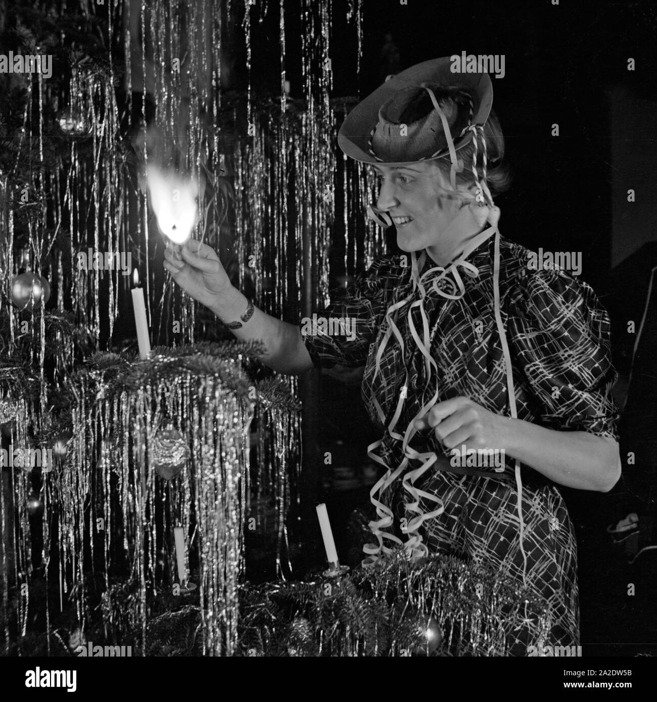 Eine junge Frau zündet die Kerzen am Tannenbaum an am Silvesterabend, Deutschland 1930er Jahre. A young woman lighting the candles at the christmas tree on new year's eve, Germany 1930s. Stock Photo