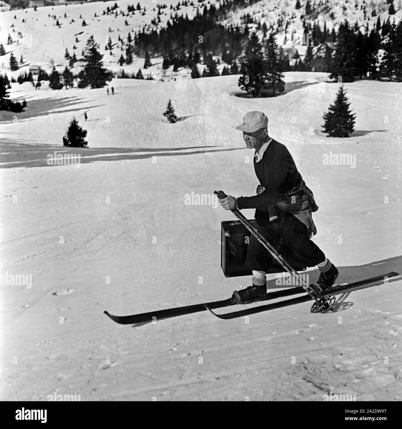 Ein Tourist kommt mit seinem Koffer auf Skiern zum Hotel, Deutschland 1930er Jahre. A tourist skiing with his suitcase to the hotel, Germany 1930s. Stock Photo