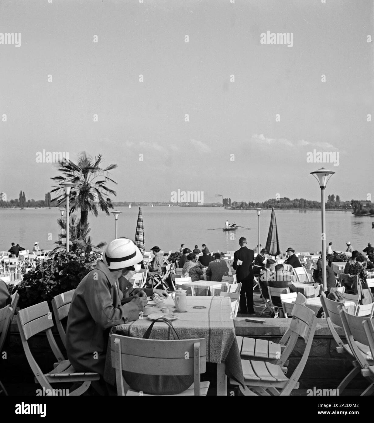 Menschen erfrischen sich in der von Palmen umgebenen Außengastronomie am Maschsee bei Hannover, Deutschland 1930er Jahre. People relaxing at a garden restaurant on the shore of Maschsee lake near Hanover, Germany 1930s. Stock Photo