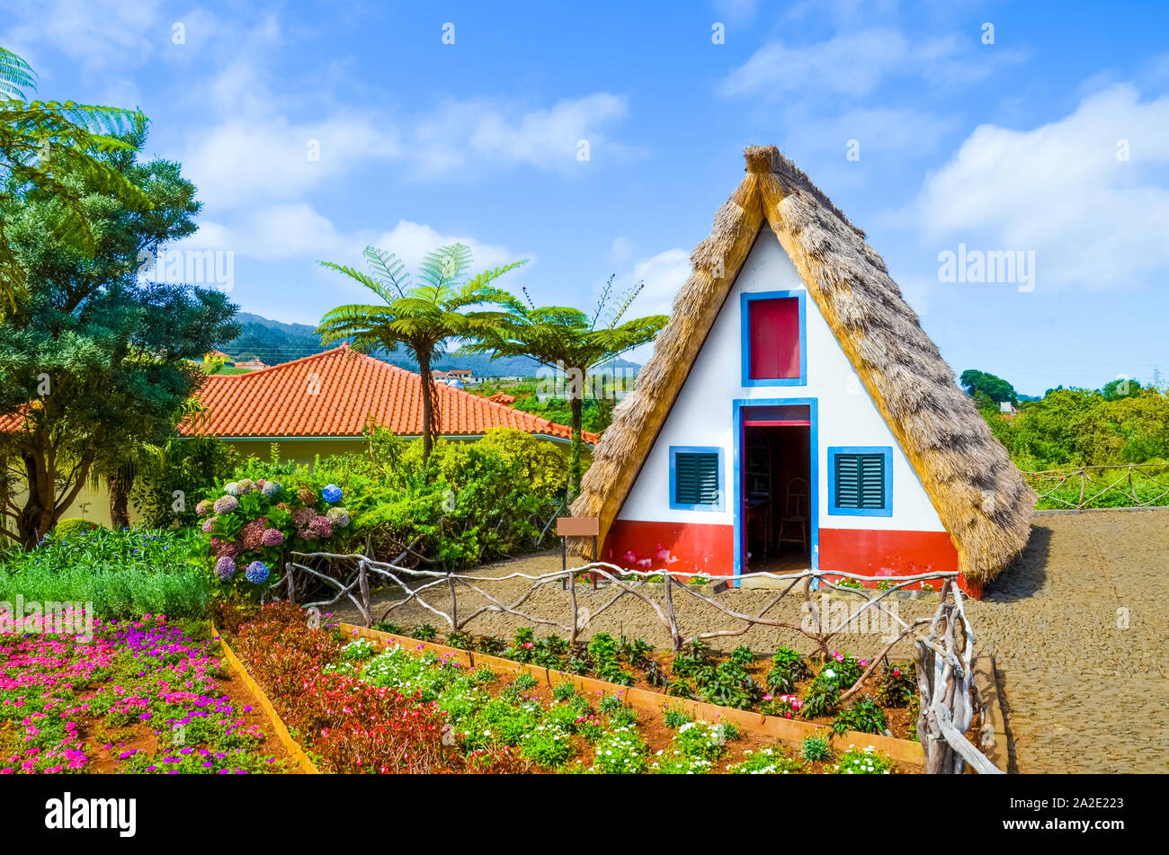 Old traditional houses in Santana, Madeira Island, Portugal. Wooden, small, triangular and colorful houses represent a part of Madeira heritage. Surrounded by flowers. Tourist attraction. Stock Photo