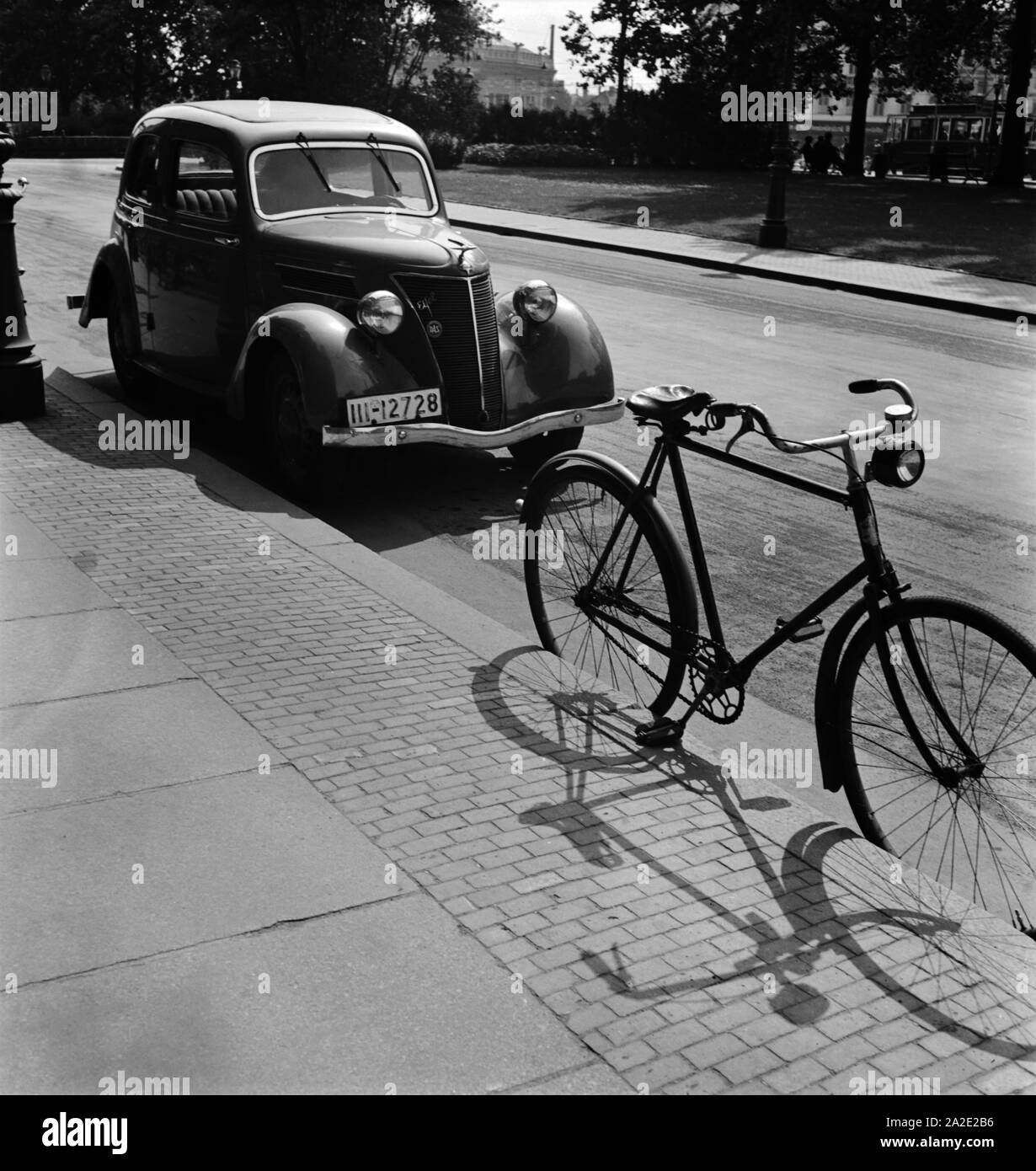 Ein Fahrrad und ein Auto parken an einem Bürgersteig in Leipzig, Deutschland 1930er Jahre. A bicycle and a car parking in a street of Leipzig, Germany 1930s. Stock Photo