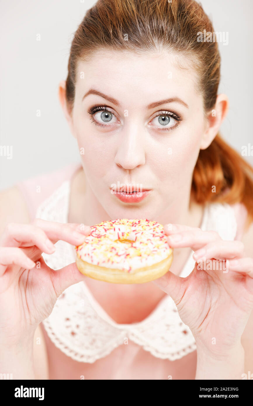 Young woman deciding whether to eat an unhealthy doughnut expressing guilt. Stock Photo