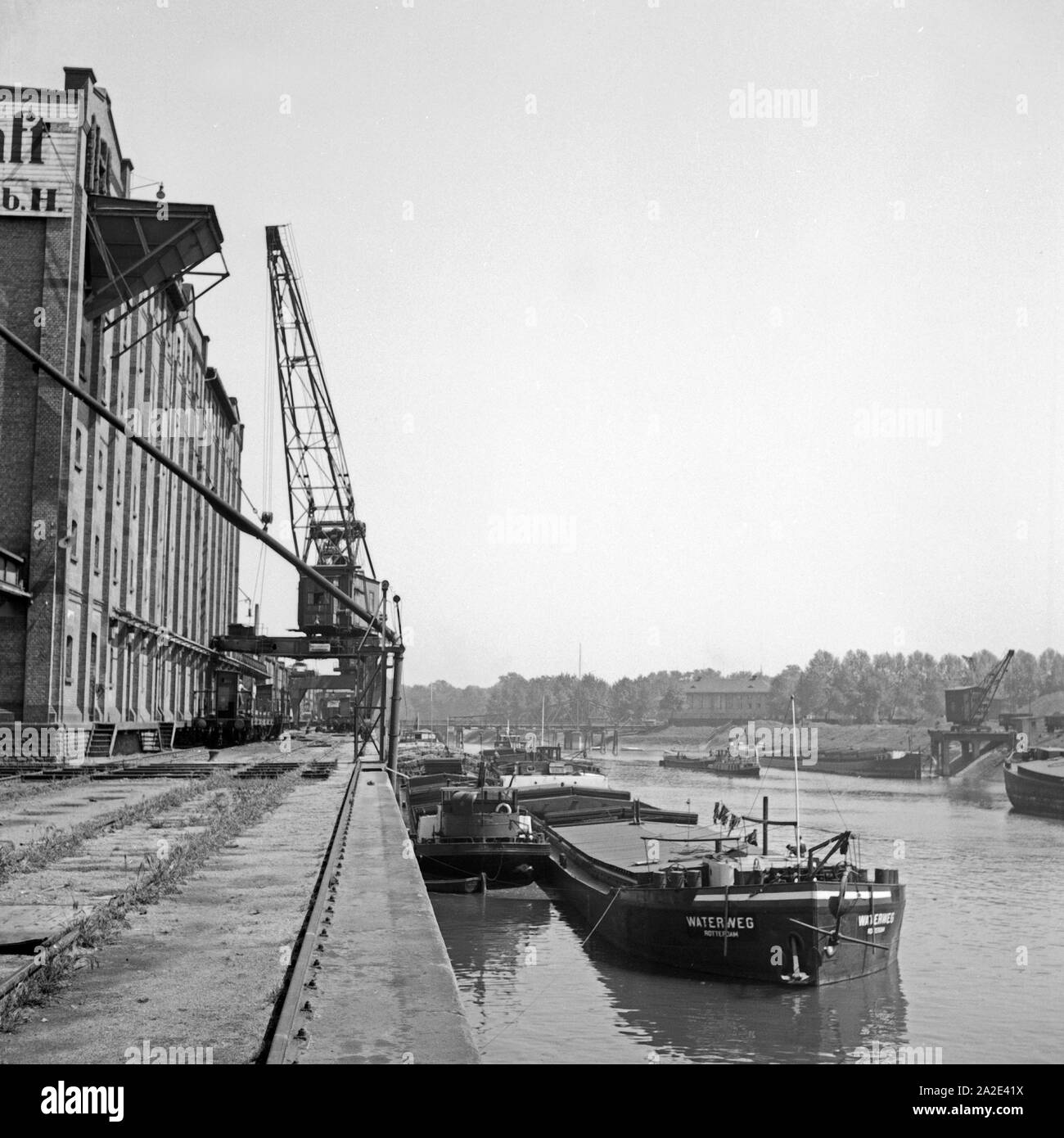 Im Hafen von Ludwigshafen am Lagerhaus der Bayerischen Transportgesellschaft werden Frachtschiffe be- und entladen, Deutschland 1930er Jahre. At the quay of the Bayerische Transportgesellschaft at Ludwigshafen harbor shop are loaded and unloaded, Germany 1930s. Stock Photo