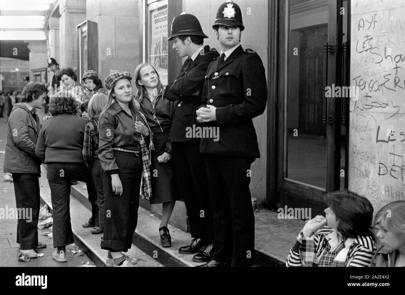 1970s UK Teenage girl Bay City Roller Fans. Boy band pop group leave pop concert at Hammersmith Odeon, west London 1975. Girls are wearing the Bay City Roller tartan fashion, chatting with policemen who are there to keep order! 70s HOMER SYKES Stock Photo