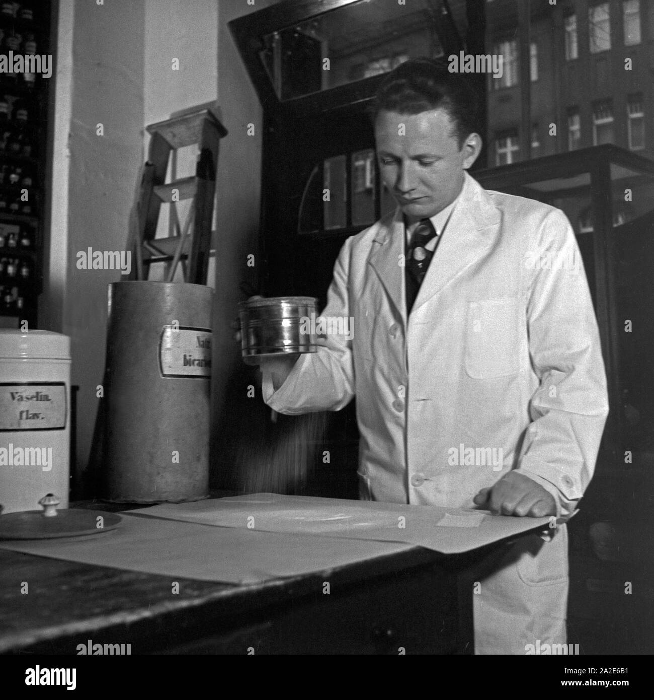 Ein Apothekerlehrling siebt einen Puder, Deutschland 1930er Jahre. A pharmacy trainee sifting and filtering powder, Germany 1930s. Stock Photo