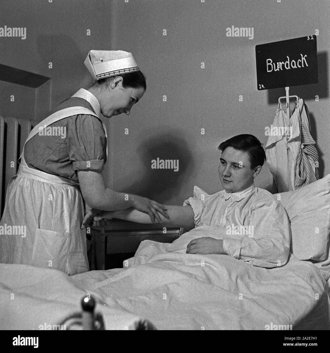 Eine junge Schwester des Deutschen Roten Kreuzes pflegt einen Patienten, Deutschland 1930er Jahre. A young nurse of the German Red Cross taking care of a sick person, Germany 1930s. Stock Photo