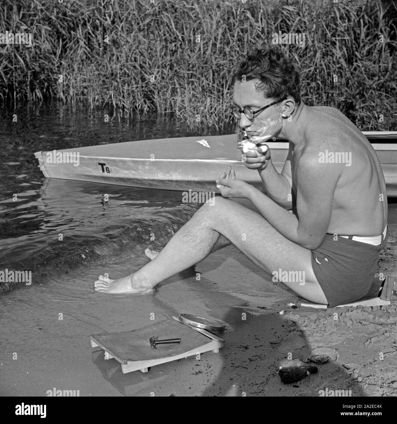 Ein junger Mann rasiert sich am Ufer eines Sees neben einem Klepper Faltboot Typ T6, Deutschland 1930er Jahre. A young man shaving at the shore of a lake, beside a Klepper folding boat, Germany 1930s. Stock Photo