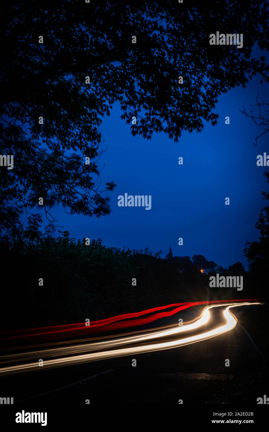 Two cars travelling opposite directions down a country road at night leaving light trails as they pass. Stock Photo