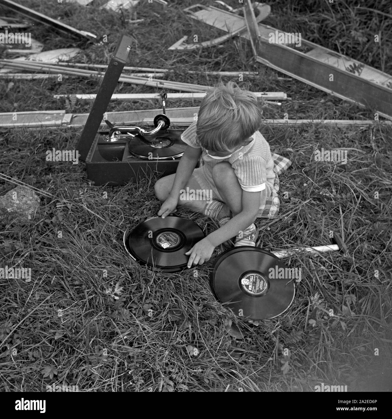 Ein kleiner Junge sortiert Schellackplatten bei einem Electrola Koffer 106 Grammophon, Deutschland 1930er J Jahre. A little boy selecting some shellack records near an Electrola Koffer 106 suitcase gramophone, Germany 1930s. Stock Photo
