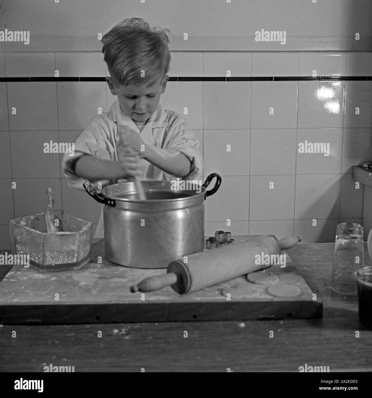 Ein kleiner Junge bereitet in der Küche einen Teig für die Weihnachtsplätzchen, Deutschland 1930er Jahre. A little boy preparing dough for christmas cookies, Germany 1930s. Stock Photo