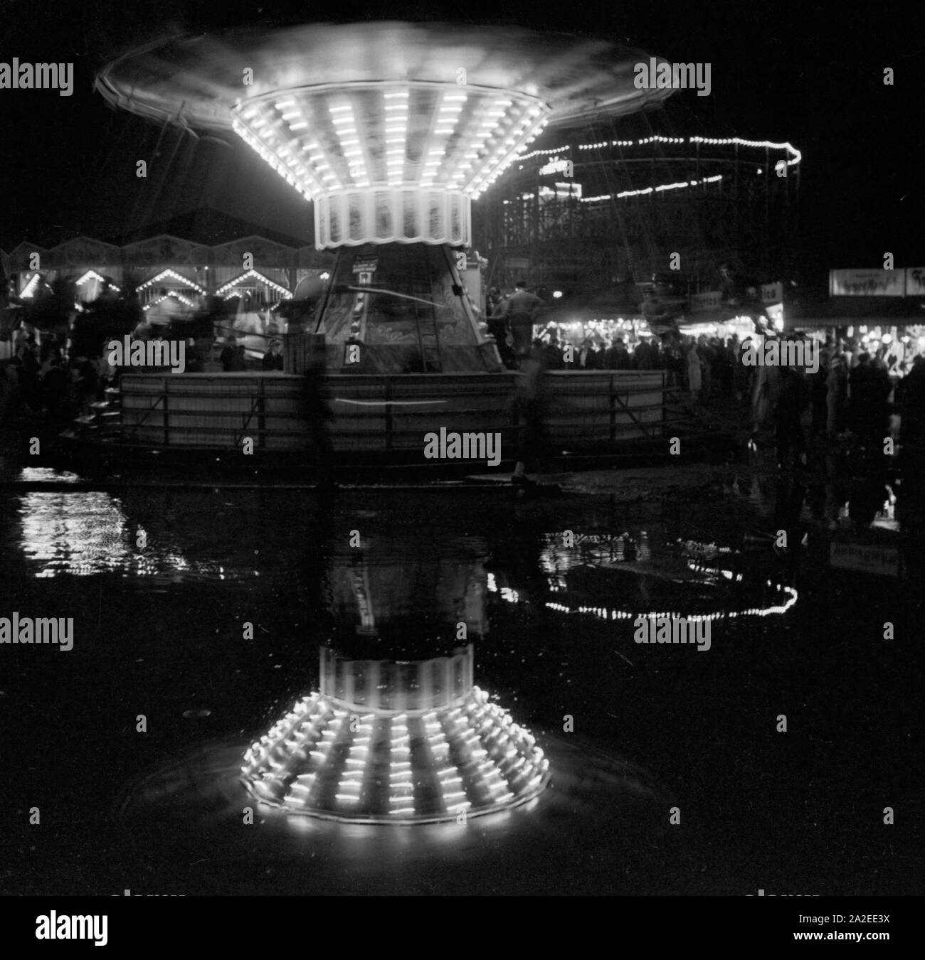 Ein Kettenkarussell spiegelt sich in einer großen Pfütze auf der Festwiese in Berlin Stralau, Deutschland 1930er Jahre. A chairoplane is reflected in a giant puddle at the Berlin Stralau annual fair, Germany 1930s. Stock Photo