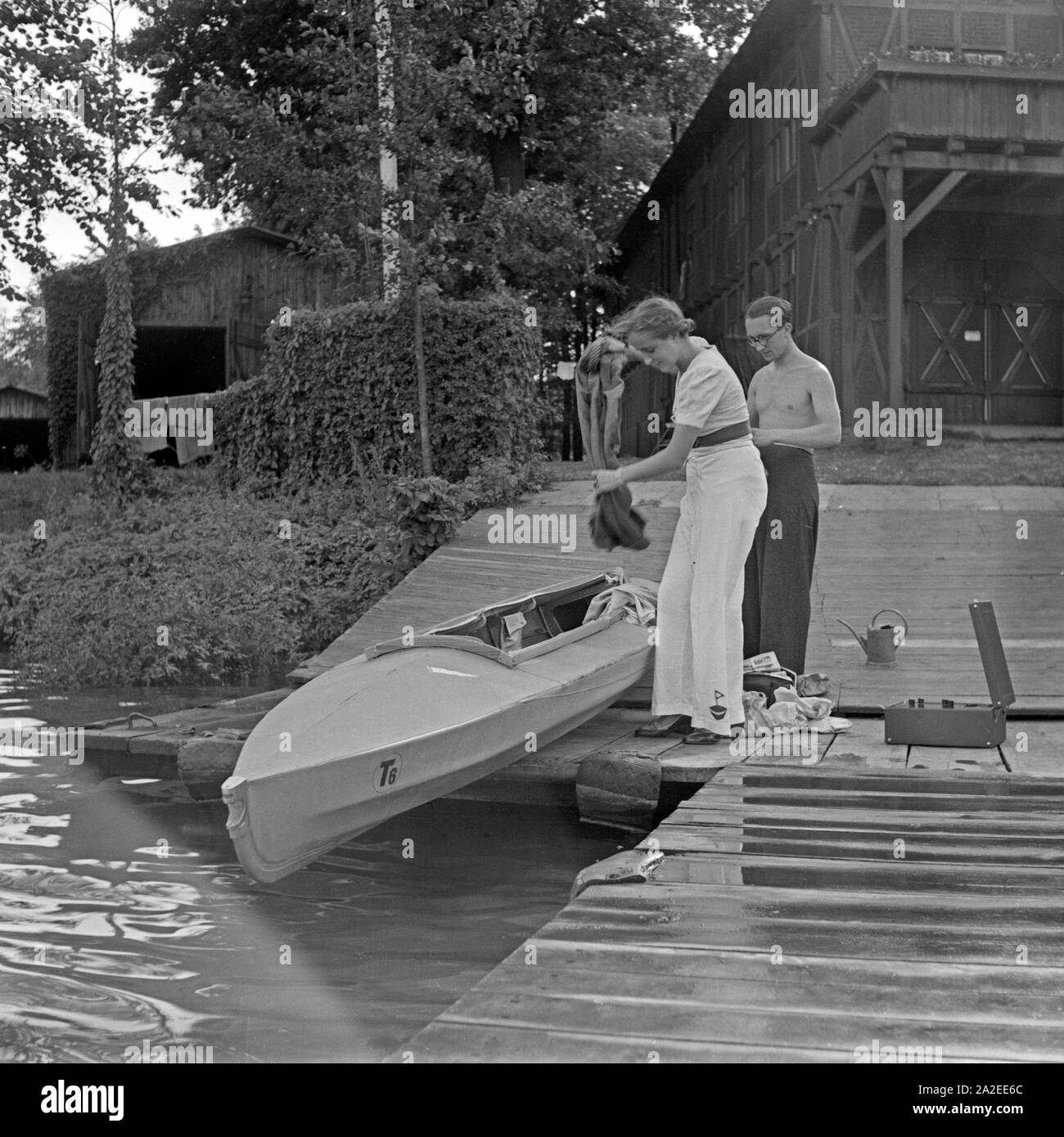 Ein junges Paar läßt ein Klepper Faltboot Typ T6 am Steg eines Sees zu Wasser, Deutschland 1930er Jahre. A young couple bringing a Klepper folding boat to the water, Germany 1930s. Stock Photo