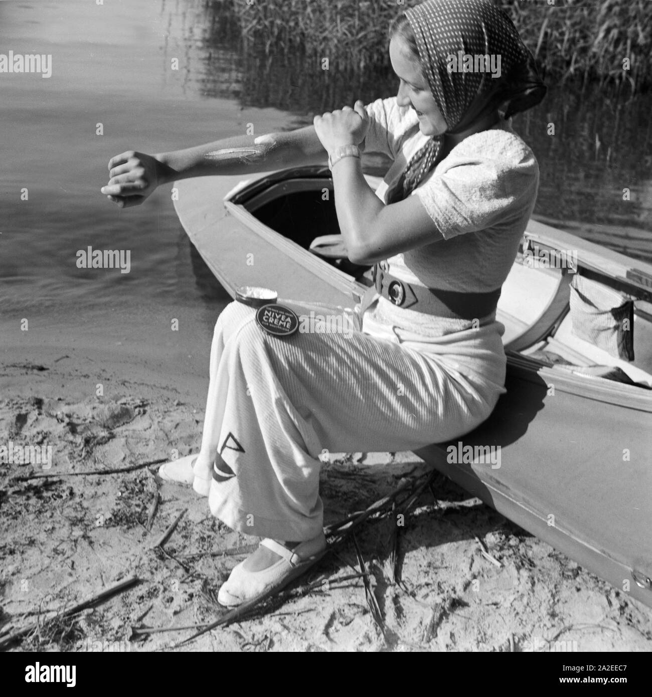 Einen guten Schutz gegen Sonnenbrand bietet Nivea Creme, eine junge Frau am  Ufer eines Sees mit einem Klepper Faltboot Typ T6, Deutschland 1930er  Jahre. A Nivea cream protects of sunburn, young woman