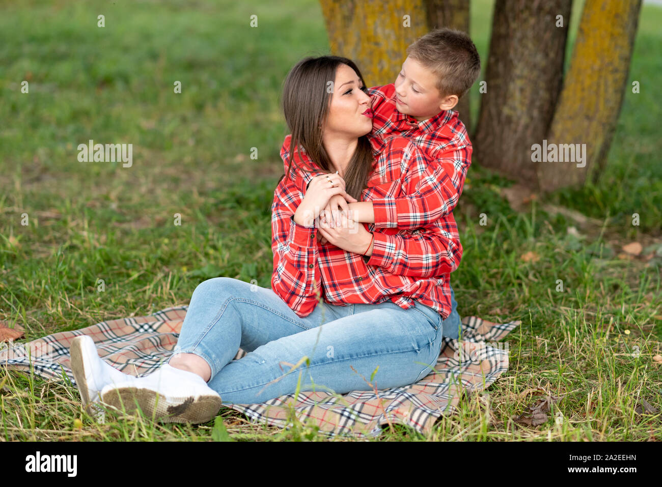 The son gently hugs mom on the shoulders, who sits on a checkered bedspread. Stock Photo