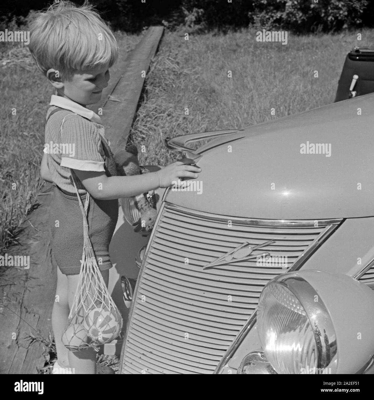 Ein kleiner Junge spielt an der Kühlerfigur am Auto seines Vaters herum, Deutschland 1930er Jahre. A little boy playing with the radiator mascot of his father's car, Germany 1930s. Stock Photo