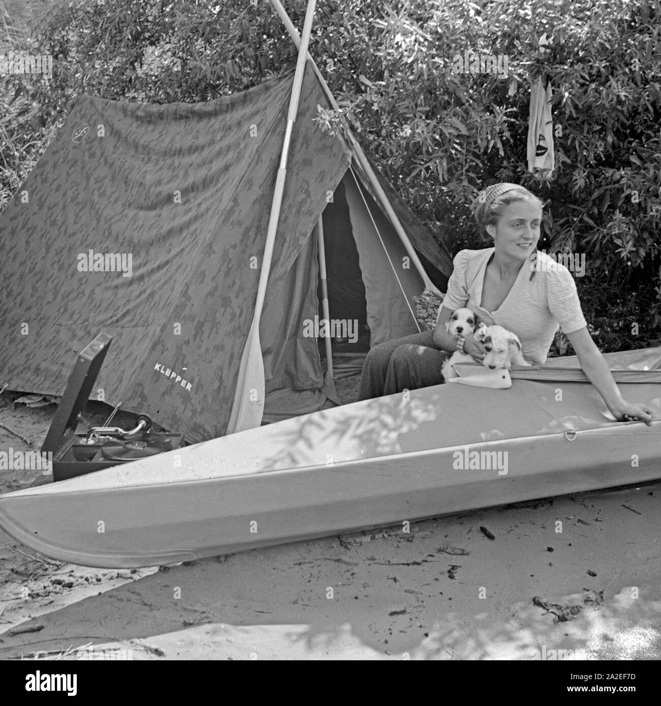 Werbefoto für das Klepper Faltboot und Zelt: eine junge Frau sitzt mit  einem Welpen vor einem Zelt und einem Boot, Deutschland 1930er Jahre.  Advertising für a Klepper foldboat and tent: a young