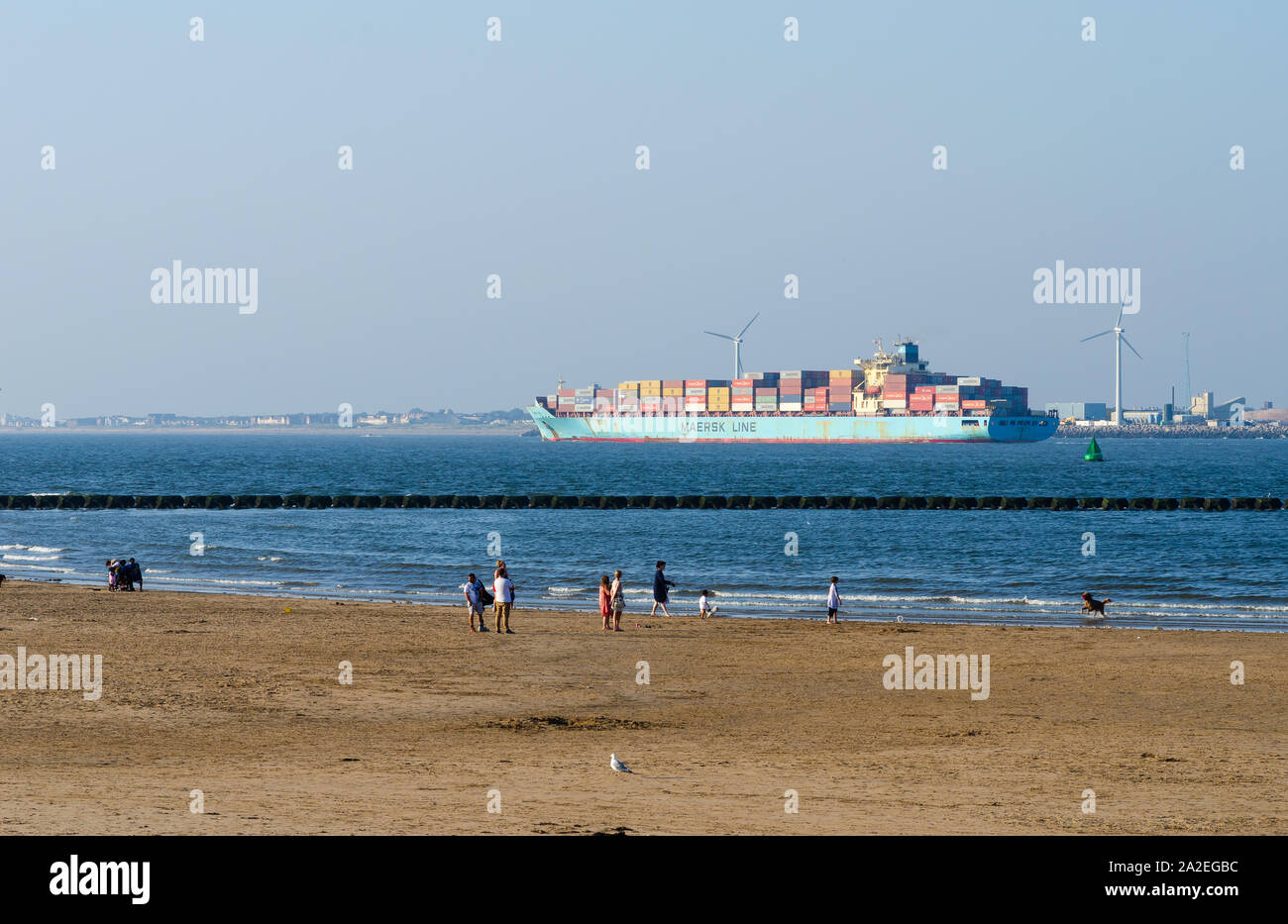 People walking on the beach on the Mersey river. 'Maersk Line' cargo ship loaded with containers is leaving Liverpool port. Stock Photo