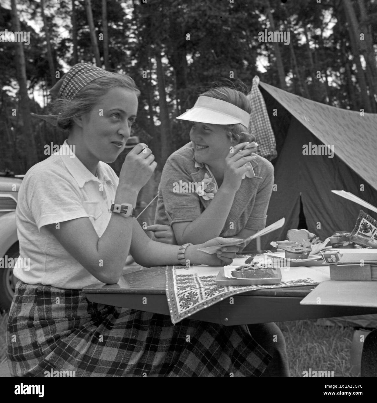 Zwei junge Frauen sitzen und essen an einem Klapptisch, Deutschland 1930er Jahre. Two young women sitting an eating at a folding table, Germany 1930s. Stock Photo