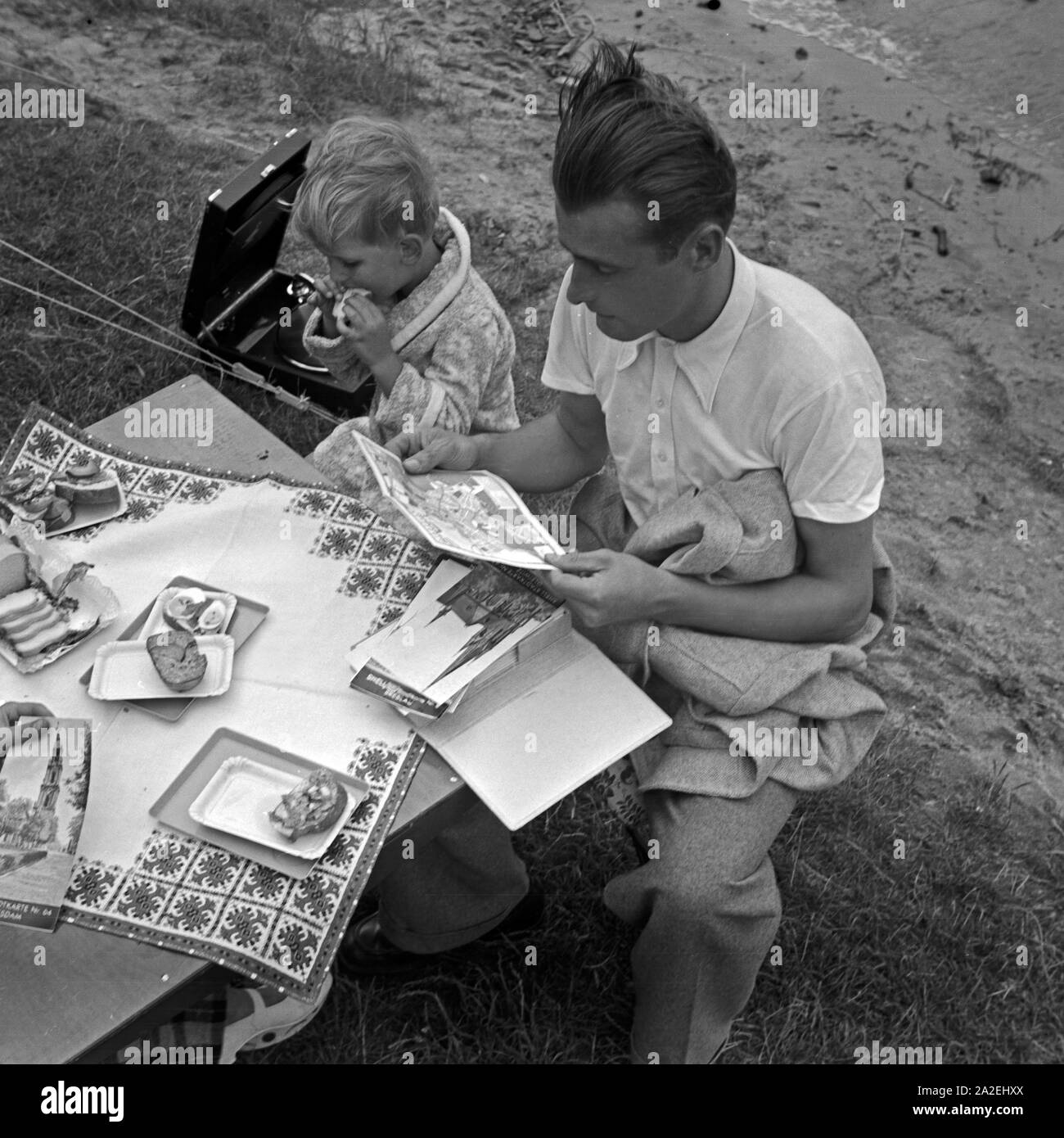 Ein Mann und ein kleiner Junge lassen es sich an einem Klapptisch schmecken, Deutschland 1930er Jahre. A man and a little boy eating at a folding table, Germany 1930s. Stock Photo