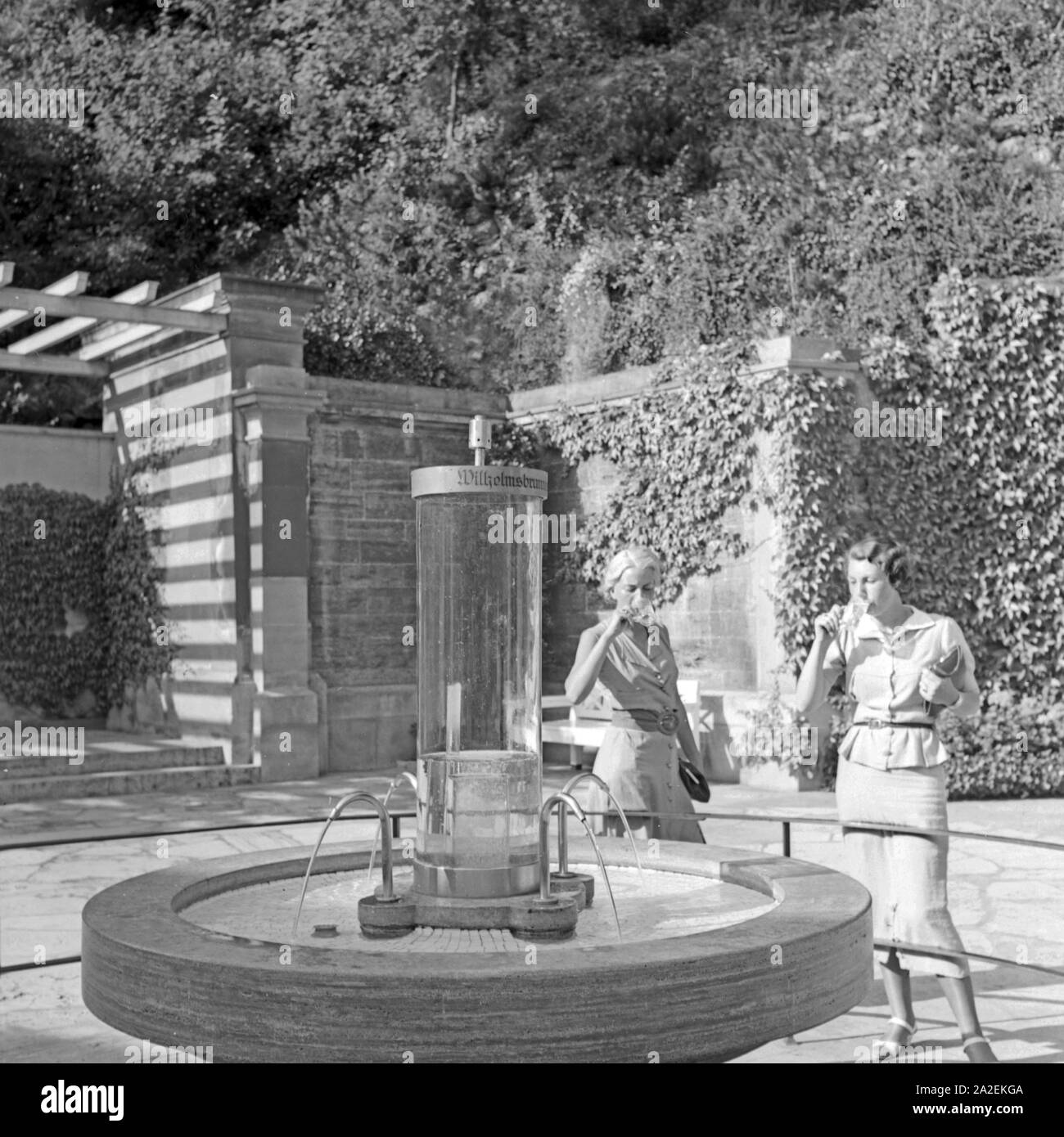 Zwei Frauen trinken aus dem Wilhelmsbrunnen in Bad Cannstatt, Deutschland 1930er Jahre. Two women drinking water from the Wilhelmsbrunnen well at Bad Cannstatt, Germany 1930s. Stock Photo