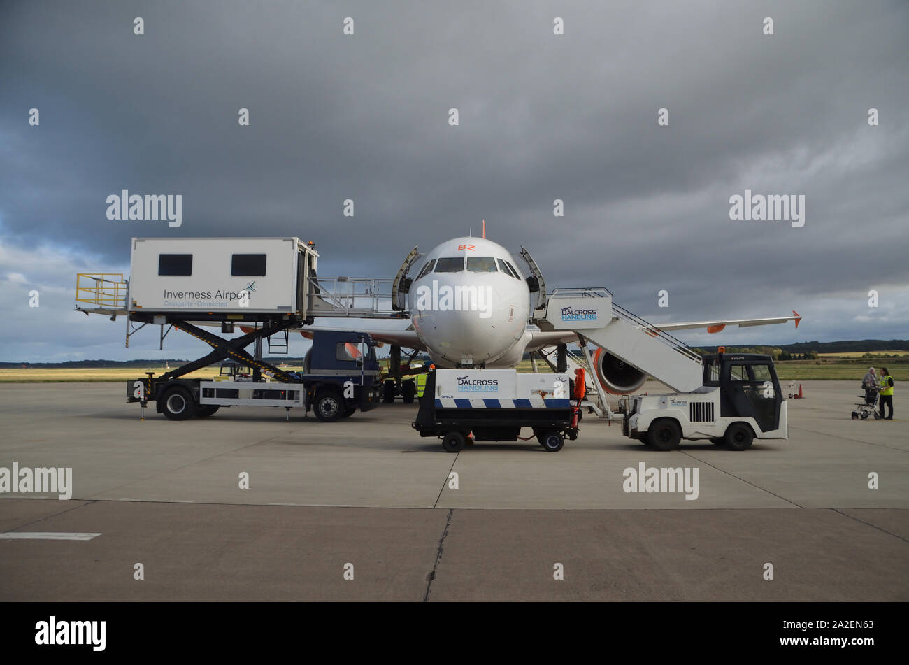An EasyJet Airbus A319-111 parked on the concrete apron surrounded by various service vehicles at Inverness Dalcross Airport, Scottish Highlands, UK. Stock Photo