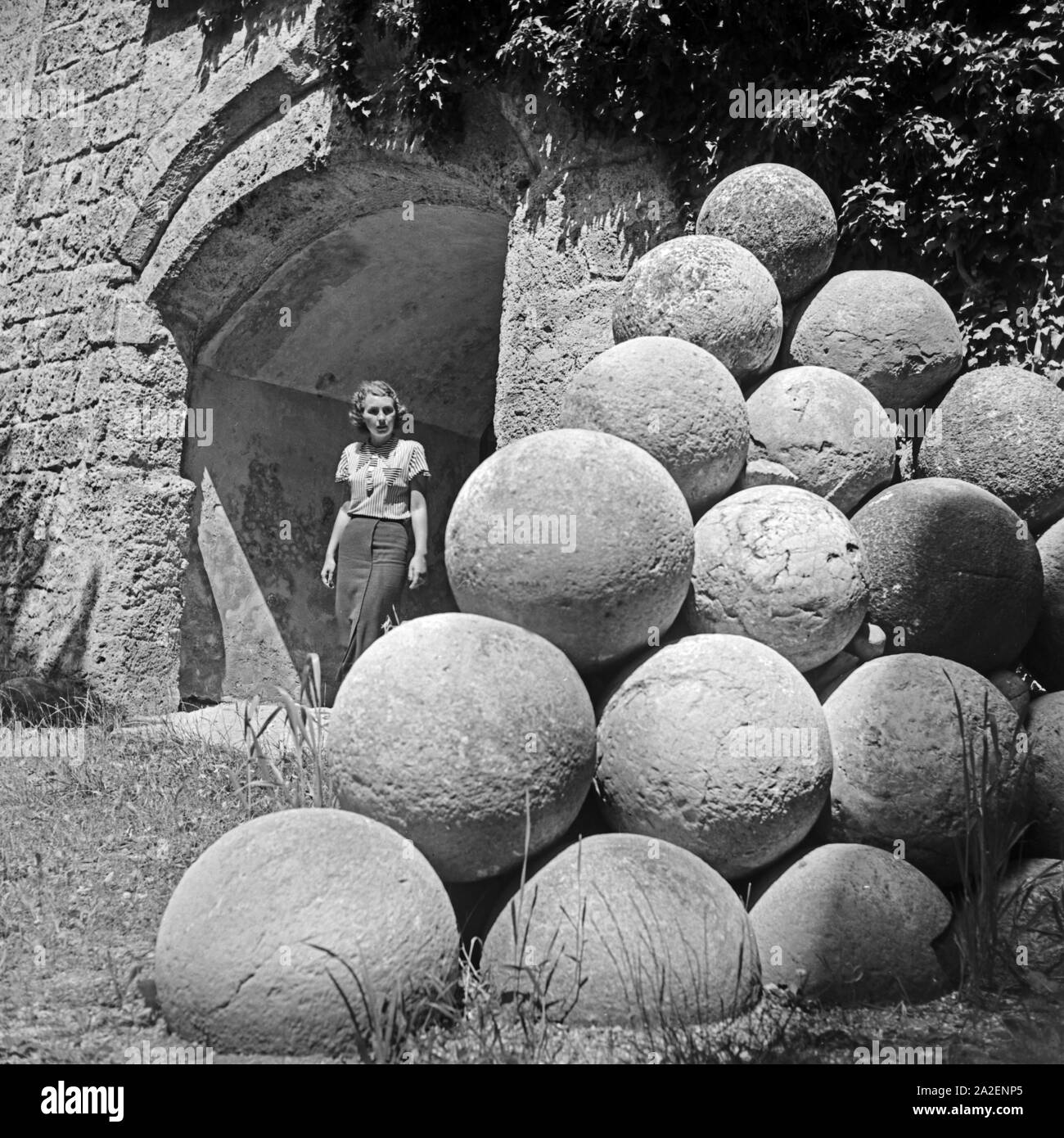 Eine Frau an einem Stapel alter Kanonenkugeln bei der Burg in Burghausen, Deutschland 1930er Jahre. A woman at old cannonballs at the old castle of Burghausen, Germany 1930s. Stock Photo