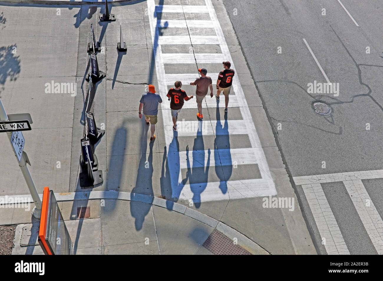 Four Cleveland Browns football fans cross a street prior to a night game casting shadows by the setting sun in downtown Cleveland, Ohio, USA. Stock Photo
