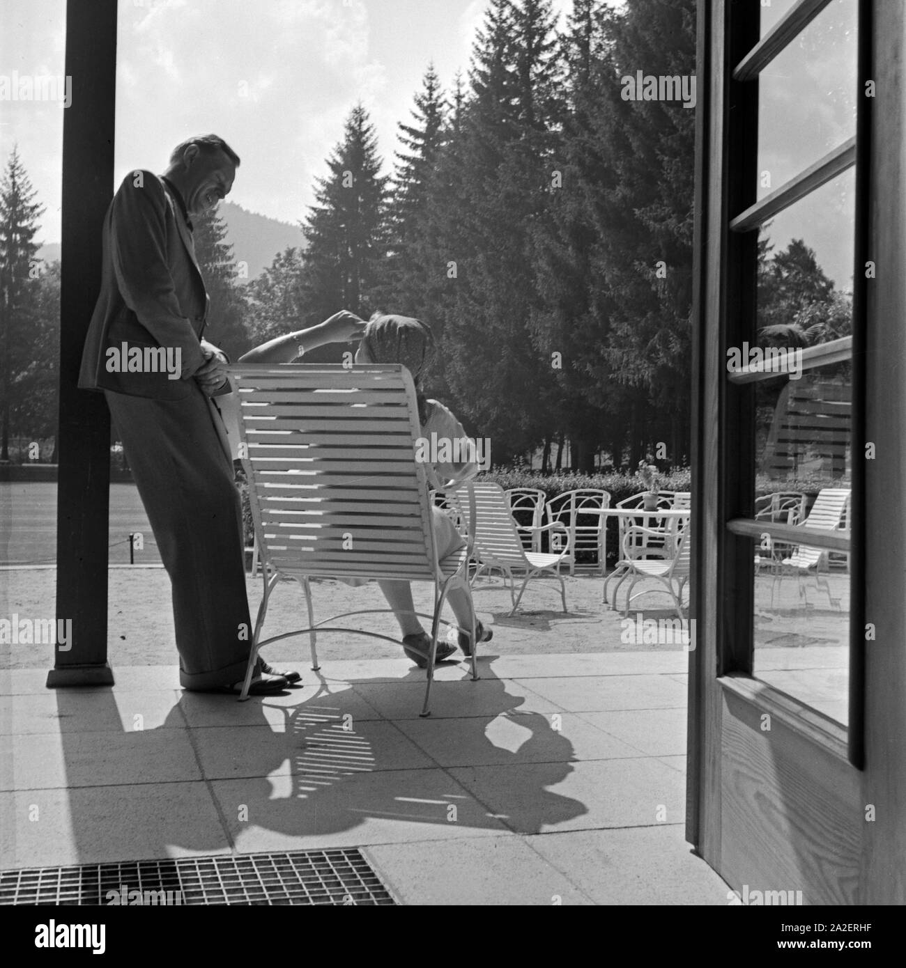 Eine Frau beim Sonnenbad auf der Terrasse am Kurhaus in Herrenalb im Schwarzwald unterhält sich mit ihrem Mann, Deutschland 1930er Jahre. A woman talking to her husband while sunbathing at the terrace of the spa resort at Herrenalb in Black Forest, Germany 1930s. Stock Photo