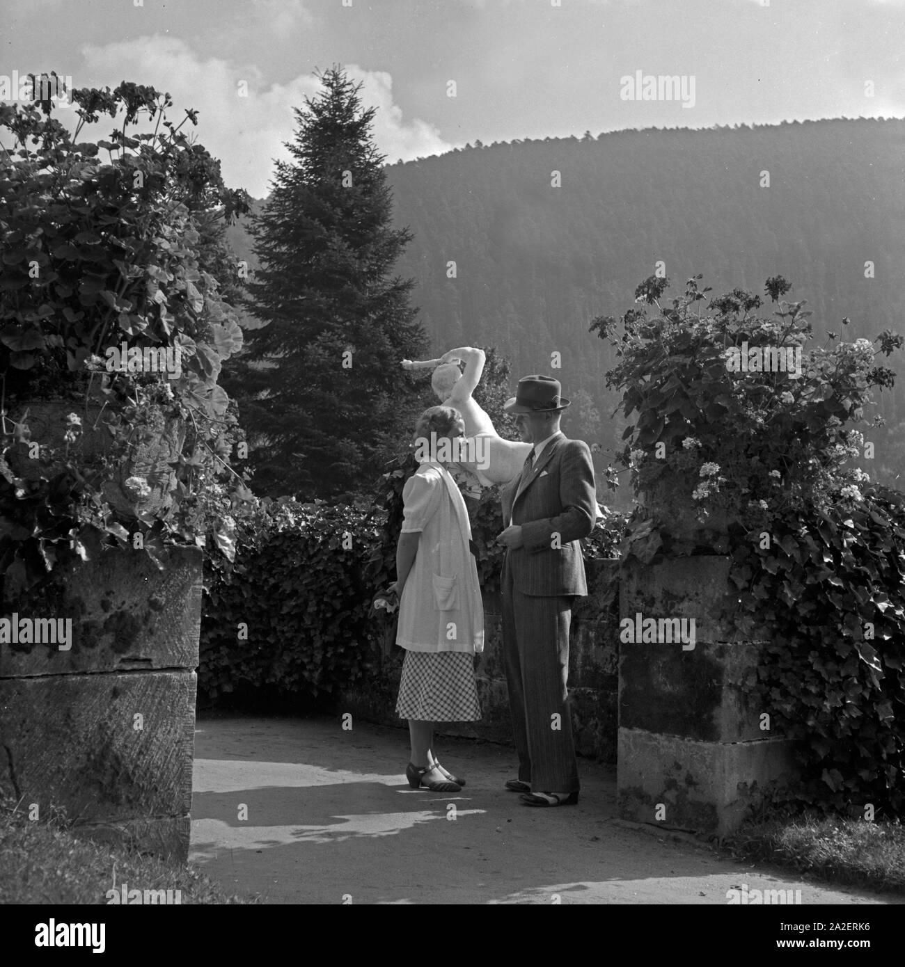 Ein Paar steht in einer Einfriedung in einem Park in Wildbad im Schwarzwald und schaut sich an, Deutschland 1930er Jahre. A couple standing in a stockade at a public park near Wildbad in Black Forest, looking at each other, Germany 1930s. Stock Photo