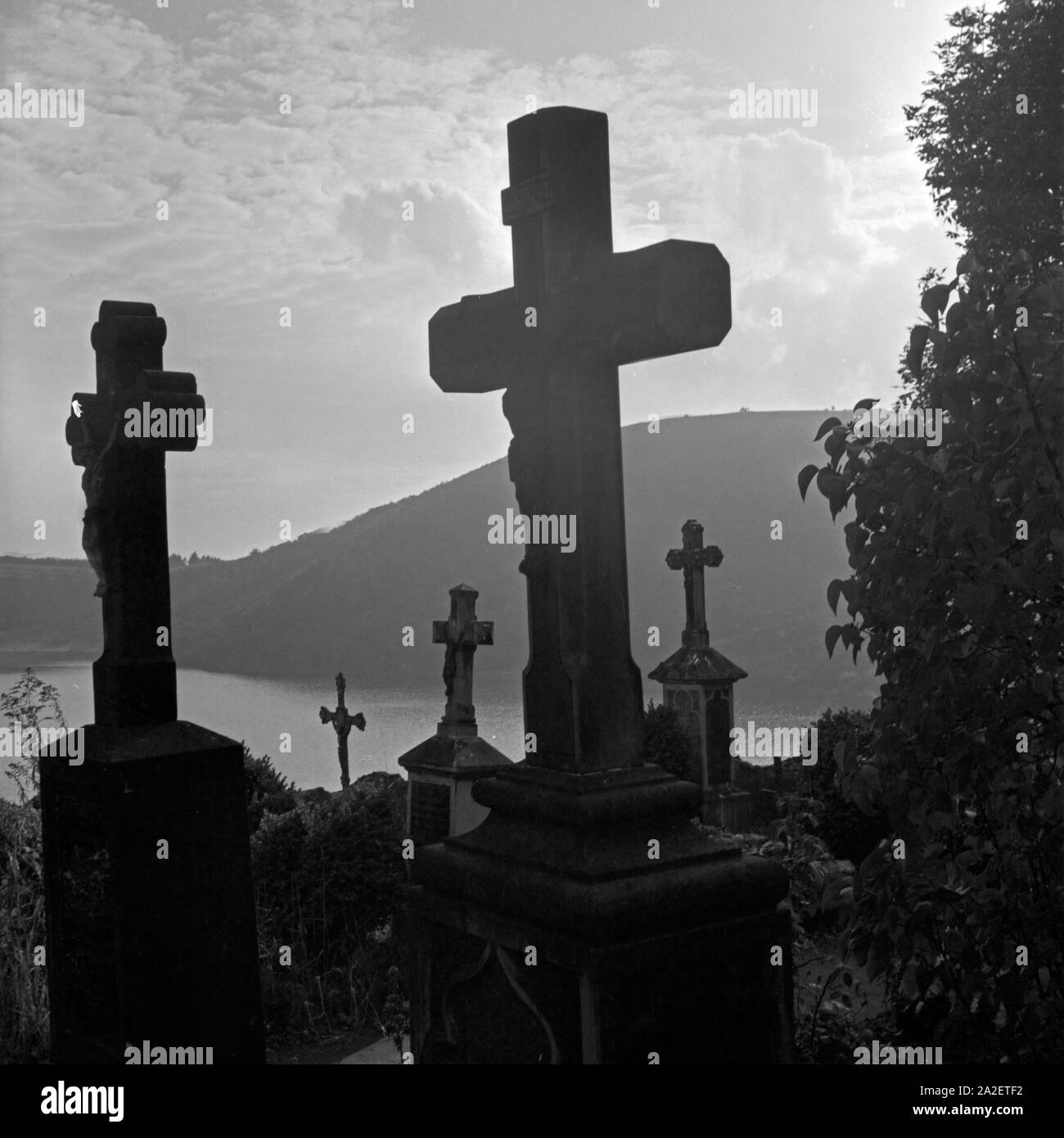 Grabkreuze auf dem Friedhof mit Blick auf das Totenmaar in Weinfeld bei Daun in der Eifel, Deutschland 1930er Jahre. Tombstones with view to Totenmaar maar lake at Weinfeld near Daun at Eifel region, Germany 1930s. Stock Photo