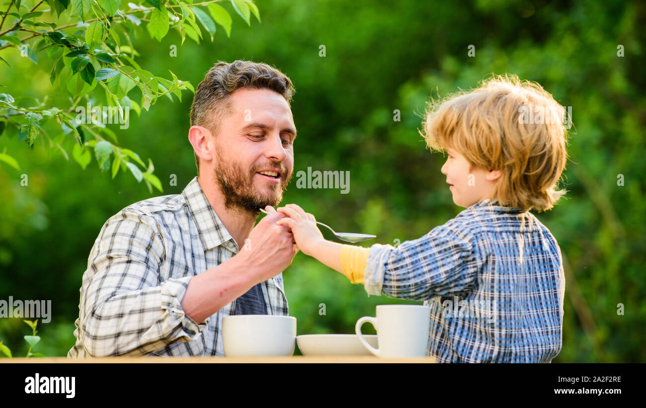 Natural nutrition concept. Feeding son natural foods. Stage of development. Feed son solids. Dad and boy eat and feed each other outdoors. Ways to dev Stock Photo