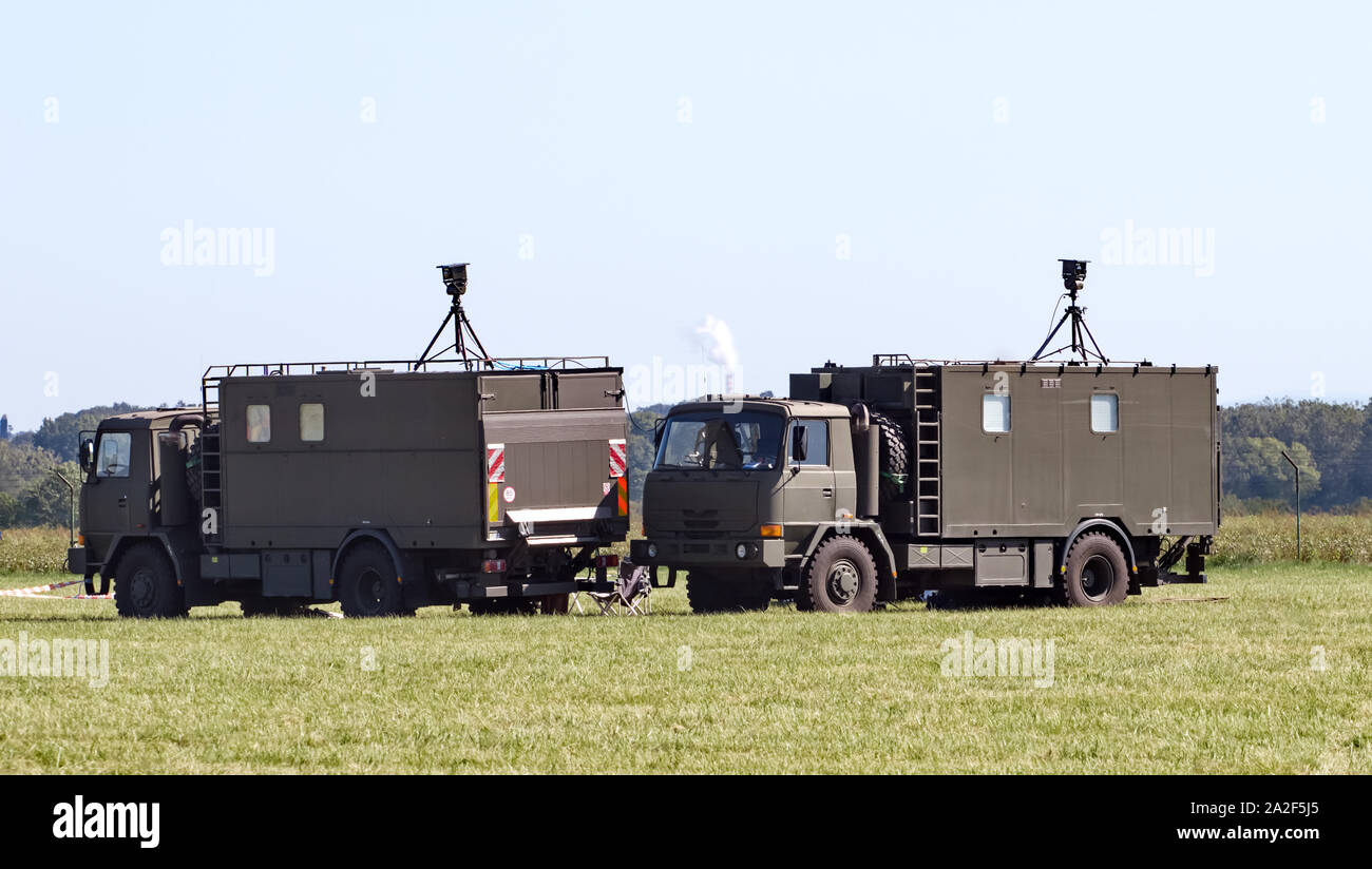 Two military command post trucks park in the field, communications equipment mounted on top. Summer day. Stock Photo