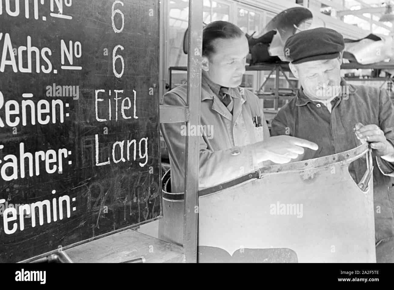 Der Autorennfahrer Hermann Lang in der Autowerkstatt im Gespräch mit einem Automechaniker, Deutschland 1930er Jahre. The racing driver Hermann Lang talking to a car mechanic in the autoshop, Germany 1930s. Stock Photo