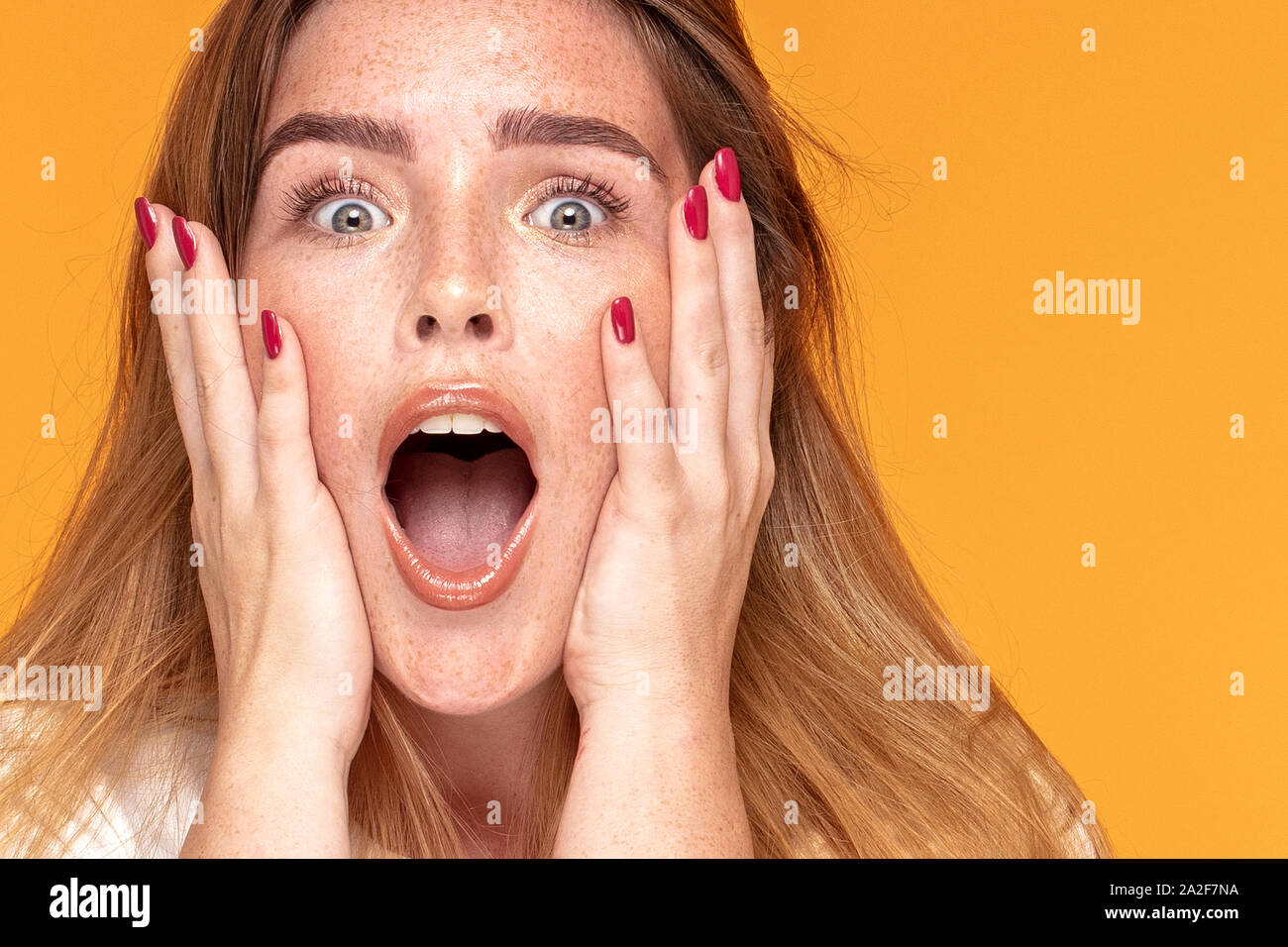 Emotional happy young ginger woman with freckles on her face . Human expression, emotions concept. Yellow color studio background. Stock Photo