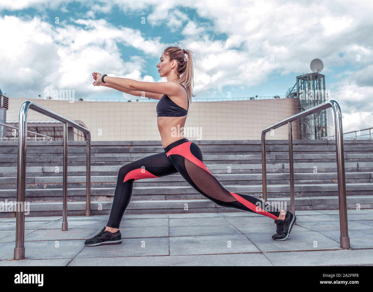 A sports girl in the city in summer does a warm-up before training,  stretching muscles, workout in the fresh air, sportswear, leggings top,  sneakers Stock Photo - Alamy