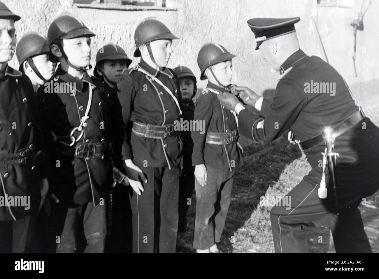 Ein Feuerwehrmann überprüft bei einer Übung der Kinderfeuerwehr ob Uniform eines Jungen richtig sitzt, Deutschland 1930er Jahre. A firefighter is checking the right fit of the uniform of a young boy during a training of the junior firefighters, Germany 1930s. Stock Photo