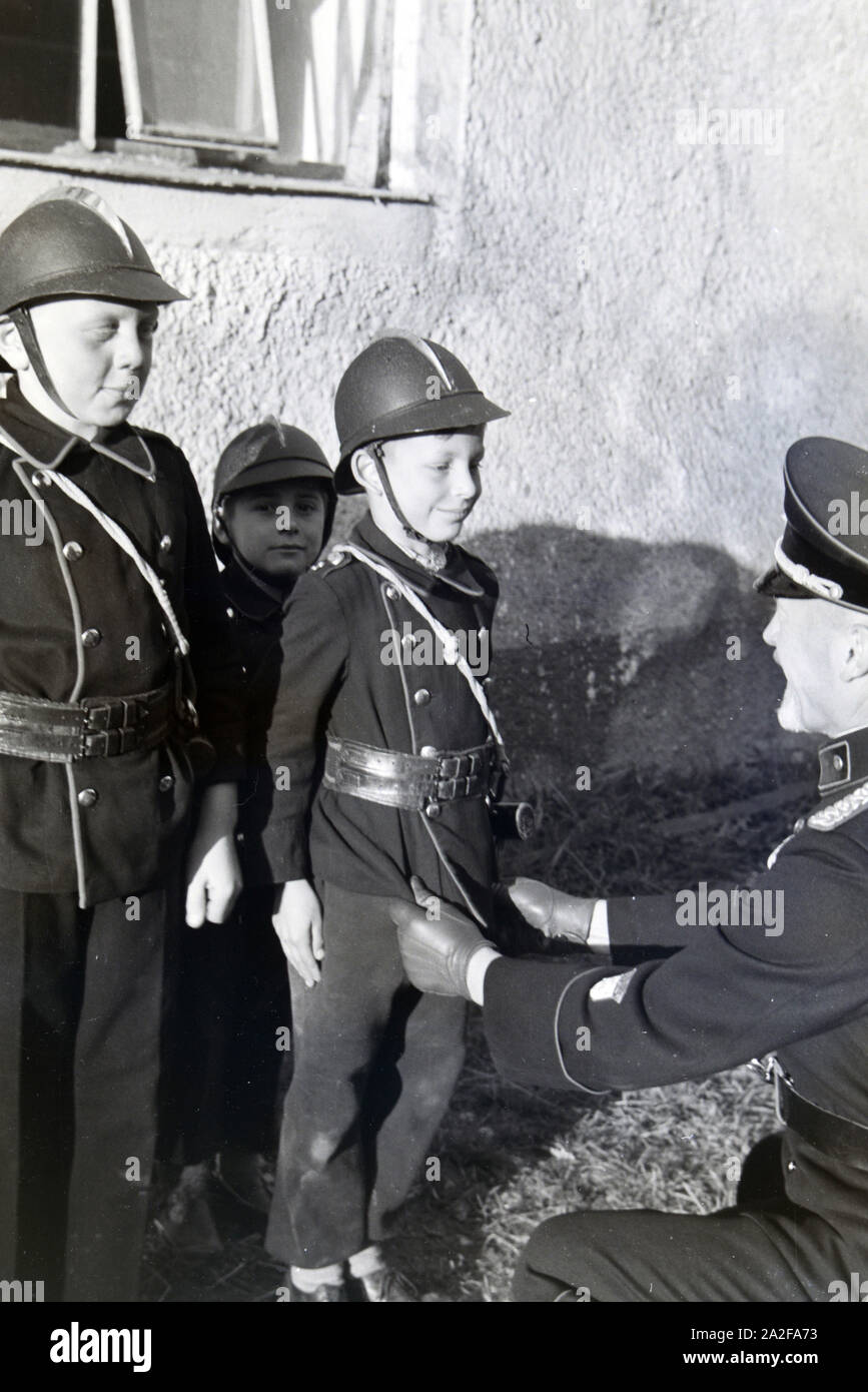 Ein Feuerwehrmann überprüft bei einer Übung der Kinderfeuerwehr ob Uniform eines Jungen richtig sitzt, Deutschland 1930er Jahre. A firefighter is checking the right fit of the uniform of a young boy during a training of the junior firefighters, Germany 1930s. Stock Photo