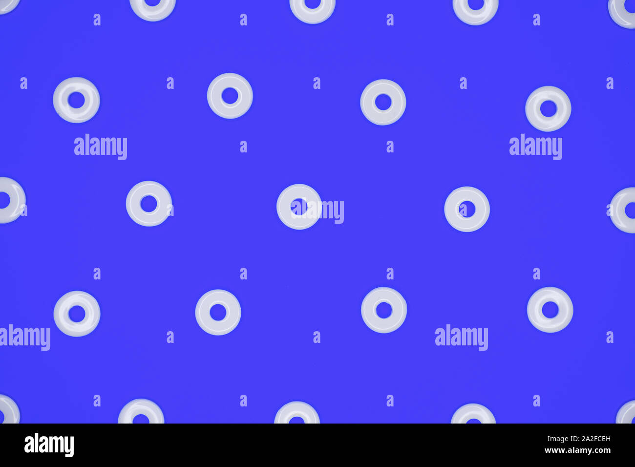 Flat round white plastic beads in regular pattern on blue cardboard background Stock Photo