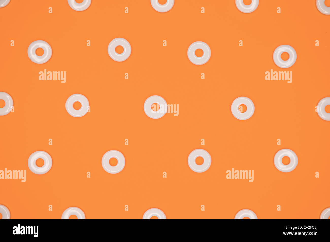 Flat round white plastic beads in regular pattern on orange cardboard background Stock Photo