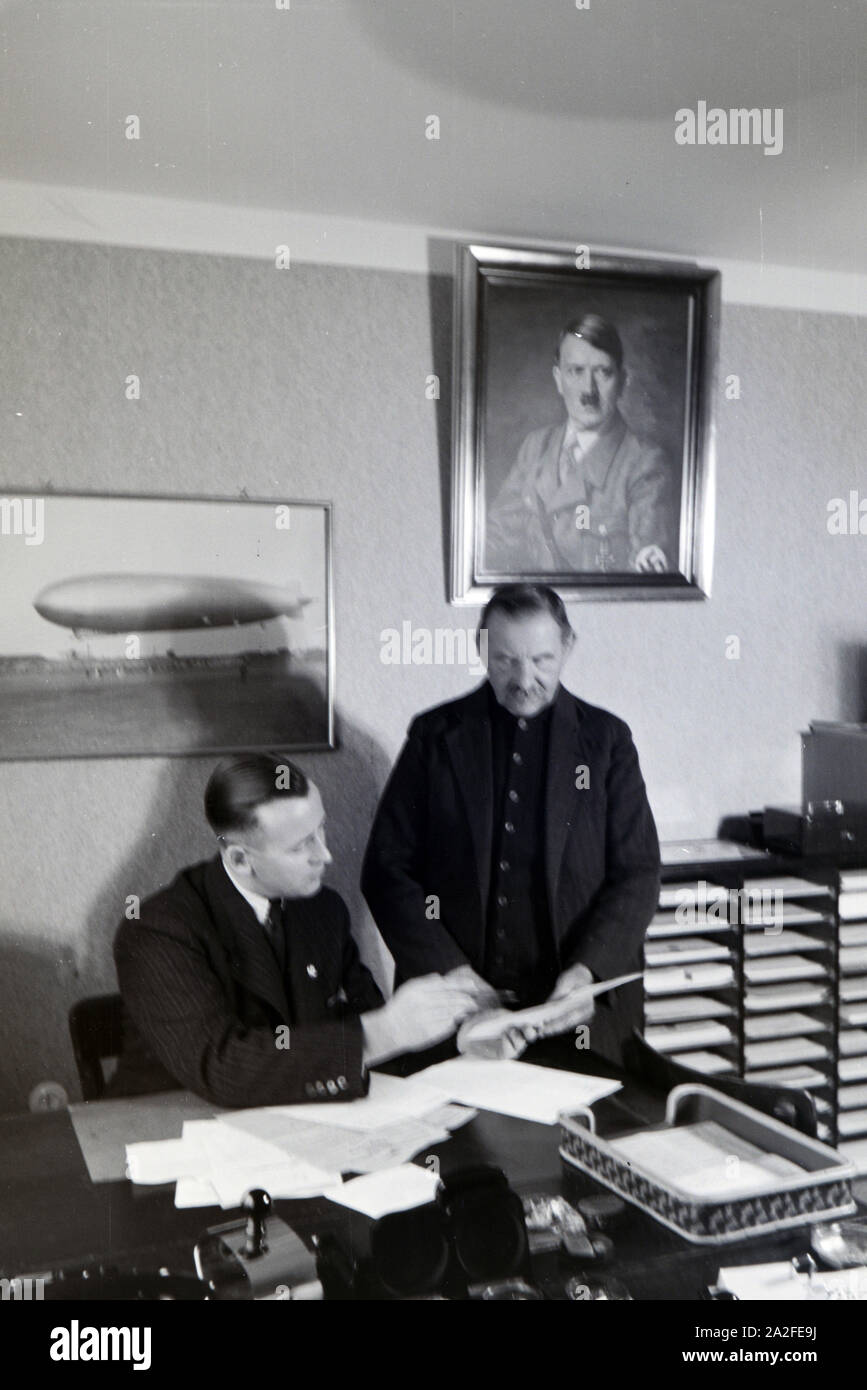 Der erste Bürgermeister der Zeppelinsiedlung, Hans von Schiller, mit einem Mitarbeiter in seinem Amtsbüdo mit einem Portrait Adolf Hitlers über dem Schreibtisch, Deutschland 1930er Jahre. The first mayor of the zeppelin village, Hans von Schiller, and an employee in his bureau with a portrait of Adolf Hitler hanging above the desk, Germany 1930s. Stock Photo