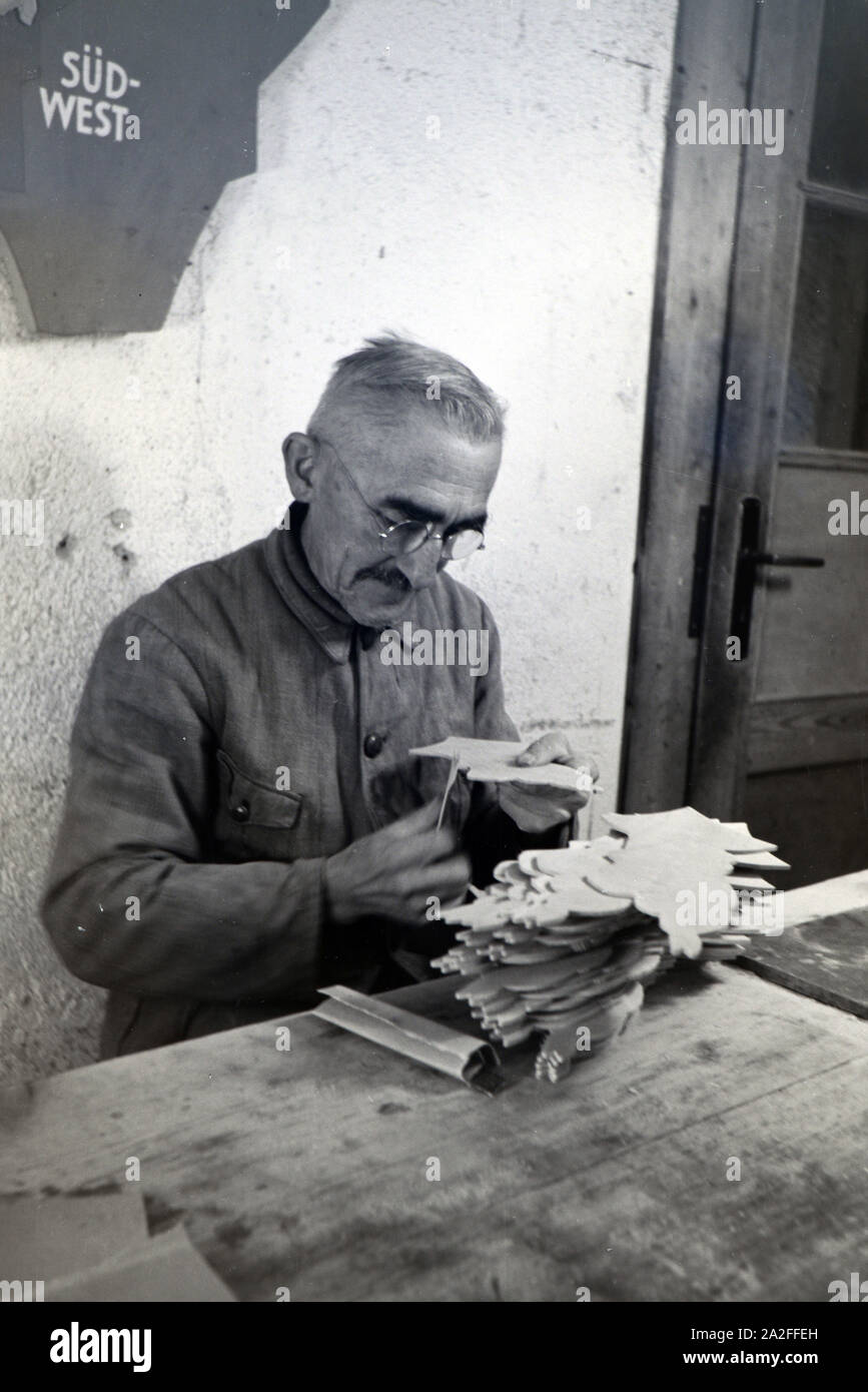 Ein Mitarbeiter in den Heller Kunst Werkstätten in der Eifel schleift die Kanten der ausgesägten Holzfiguren ab, Deutschland 1930er Jahre. An employee of the Heller Kunst workshops in the Eifel grinding the edges of the sawn out wooden figures, Germany 1930s. Stock Photo