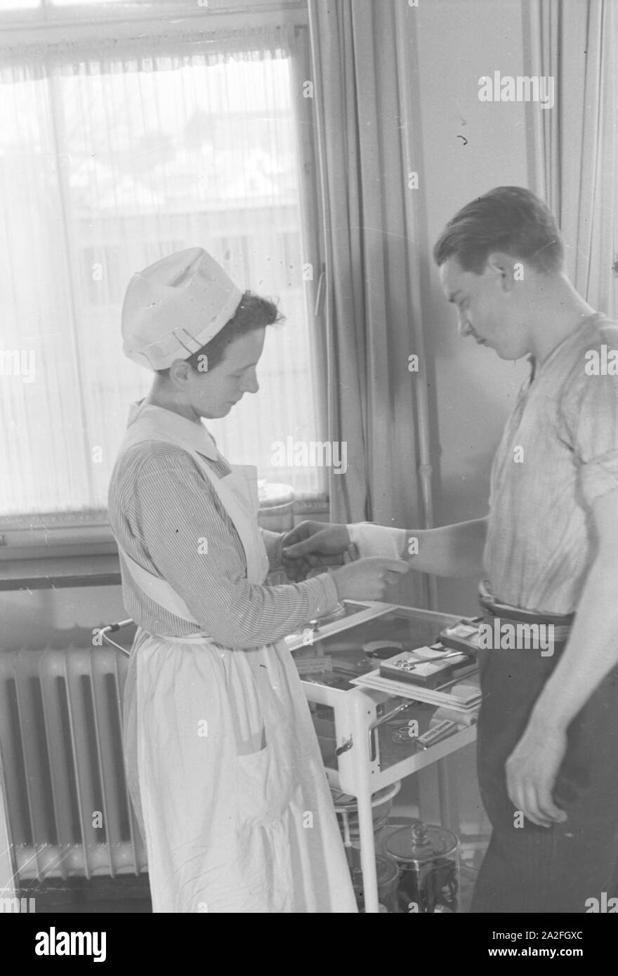 Eine Krankenschwester vebindet das verletzte handgelenk eines jungen Mannes, Deutschland 1930er Jahre. A nurse is patching up the wounded wrist of a young man, Germany 1930s. Stock Photo