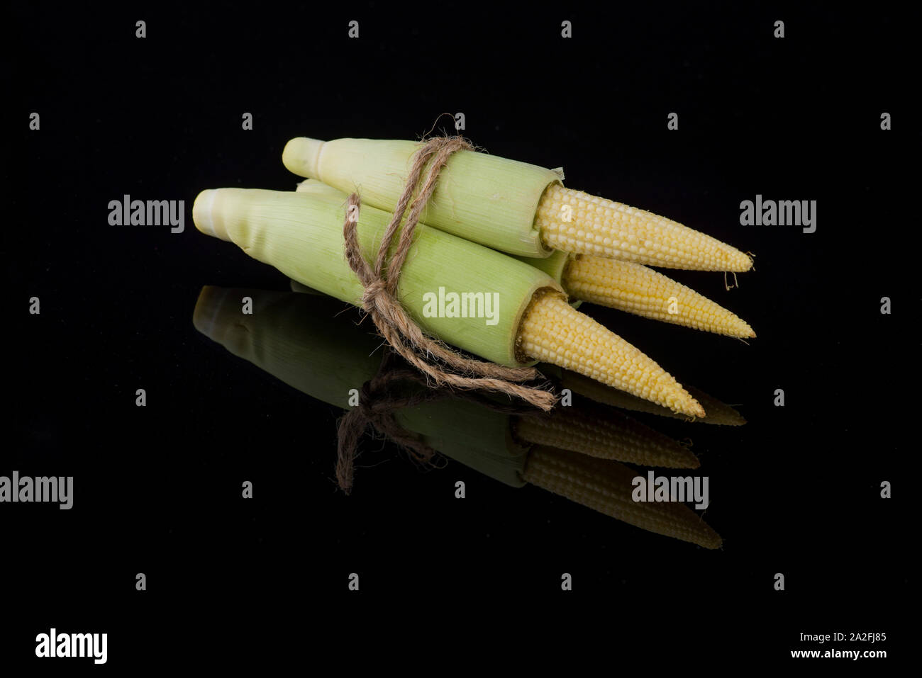 Young raw baby corn isolated on black background with small reflection ...
