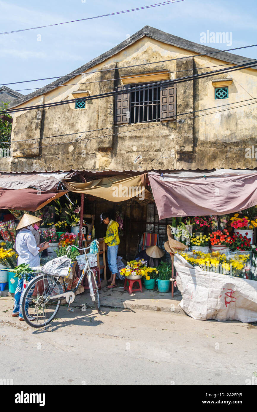 Hoi An, Vietnam - March 3rd 2010: Woman with bicycle outside a flower shop. Cycling is still a popular form of transport. Stock Photo