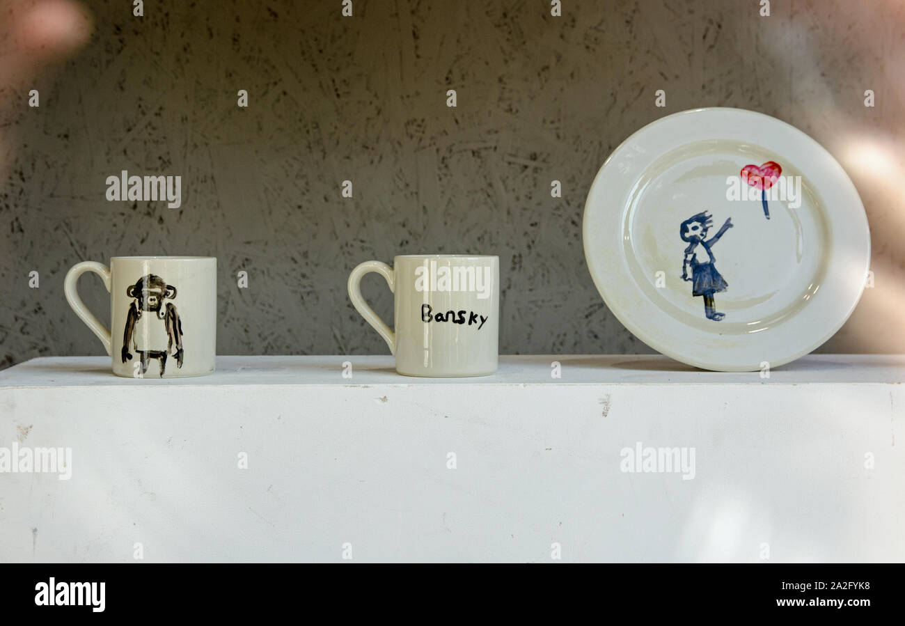 Banksy crockery, painted with spelling errors by children and on public display as part of the Gross Domestic Product exhibition in a shop window in C Stock Photo