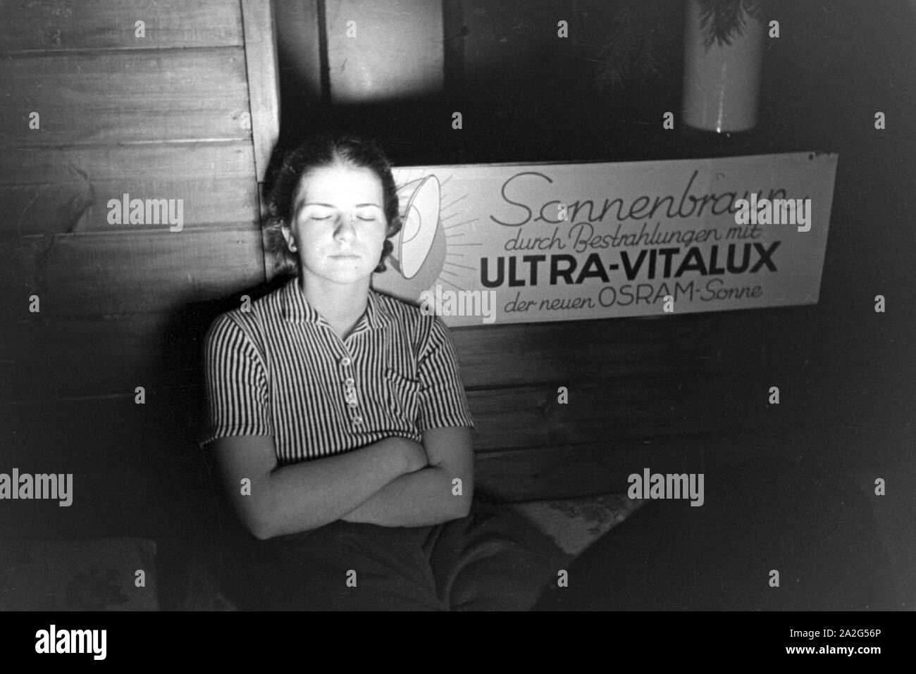 Eine junge Frau nimmt ein Sonnenbad vor der Lampe einer Höhensonne der Firma Ultra Vitalux mit der neuen Osram Lampe, Deutschland 1930er Jahre. A young woman tanning with the new Ultra Vitalux sunlamp, Germany 1930s. Stock Photo