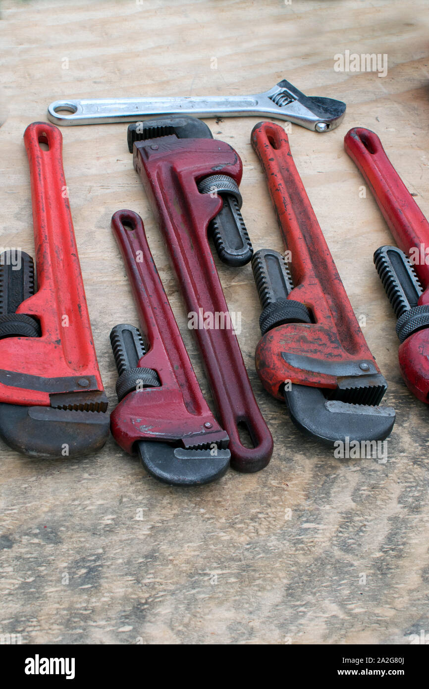 A row of pipe wrenches and an adjustable wrench are laid out on plywood at a garage sale Stock Photo